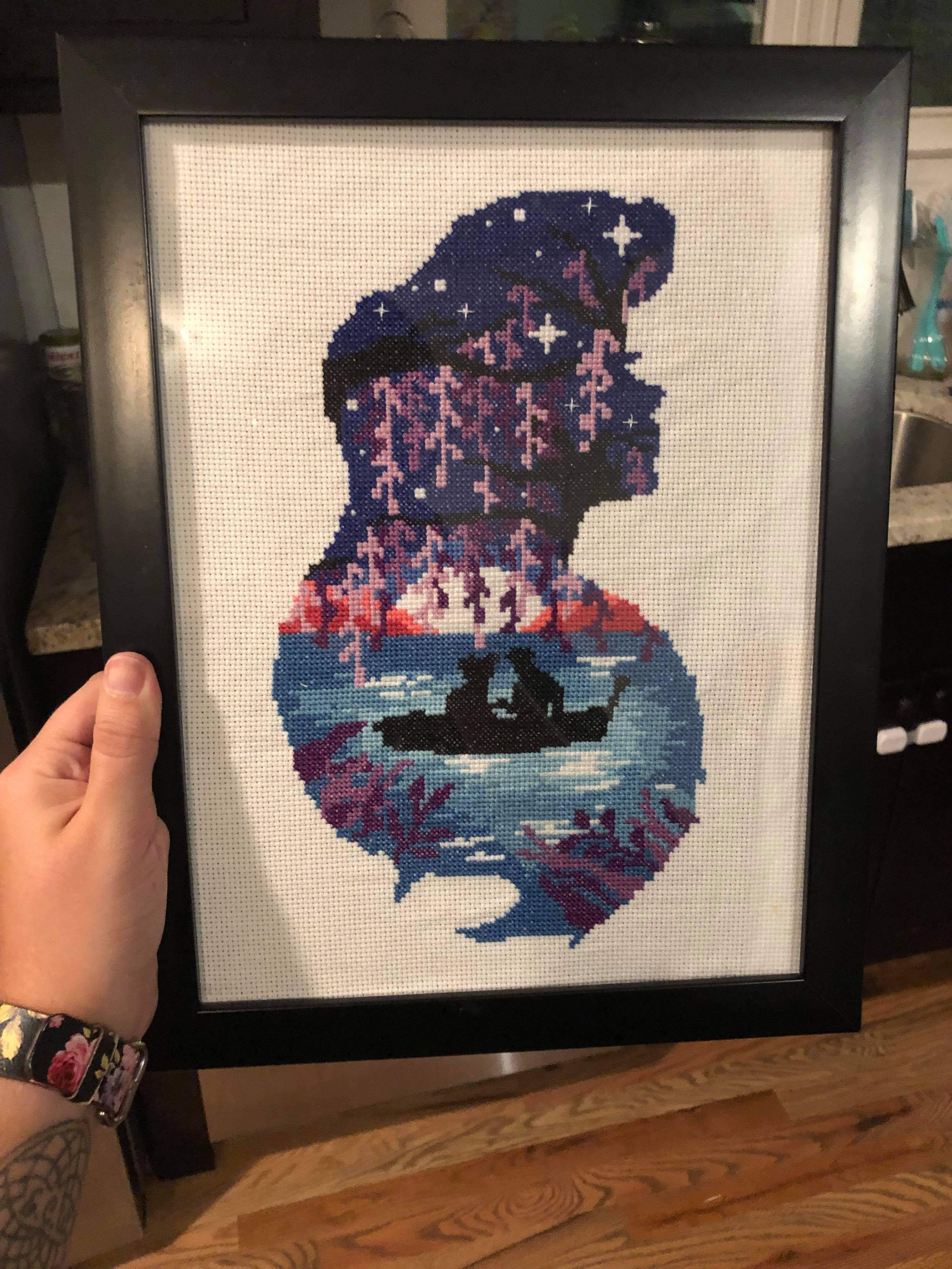 A cross stitch in the shape of ariel's head with the kiss the girl scene filling it out